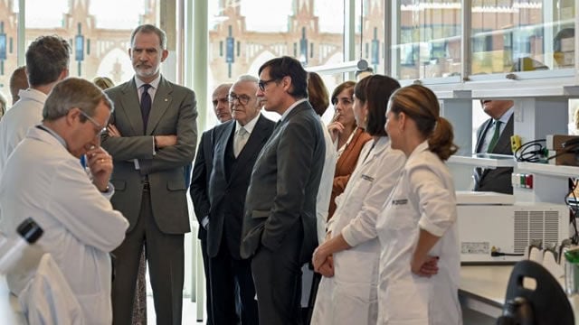 S. M. el Rey, Isidro Fain&eacute; y Salvador Illa escuchando a los investigadores del CaixaResearch Institute.